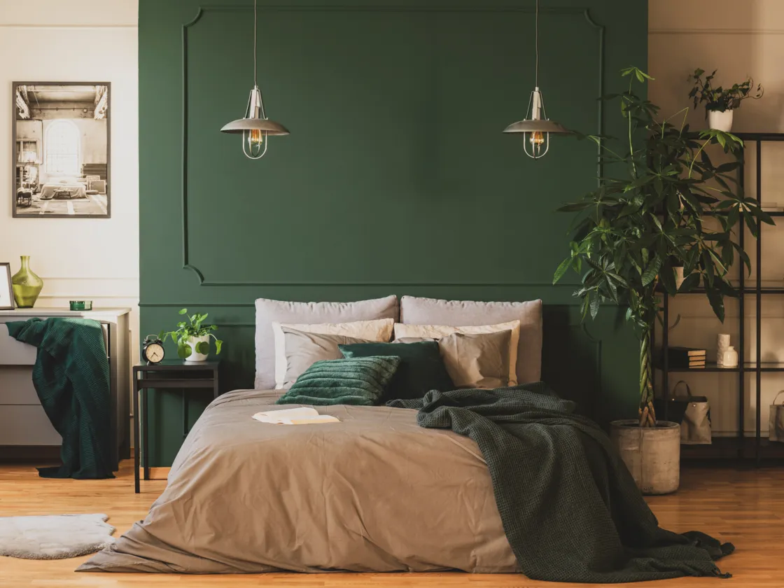 A nature-inspired bedroom with a striking green accent wall complemented by lush plants and plush pillows